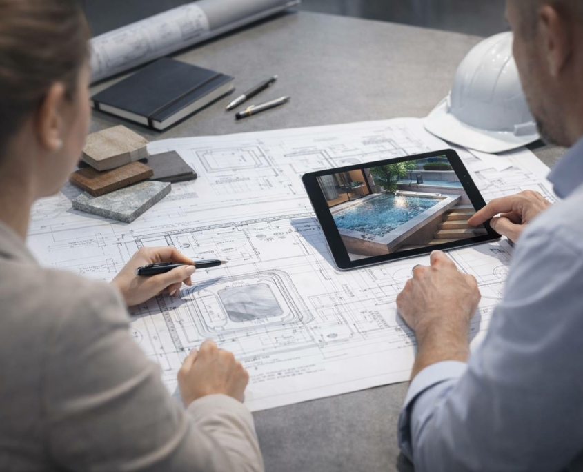 Réunion technique : architecte et ingénieur analysent un plan d’espace spa avec tablette affichant une vue 3D, échantillons bois et pierre.